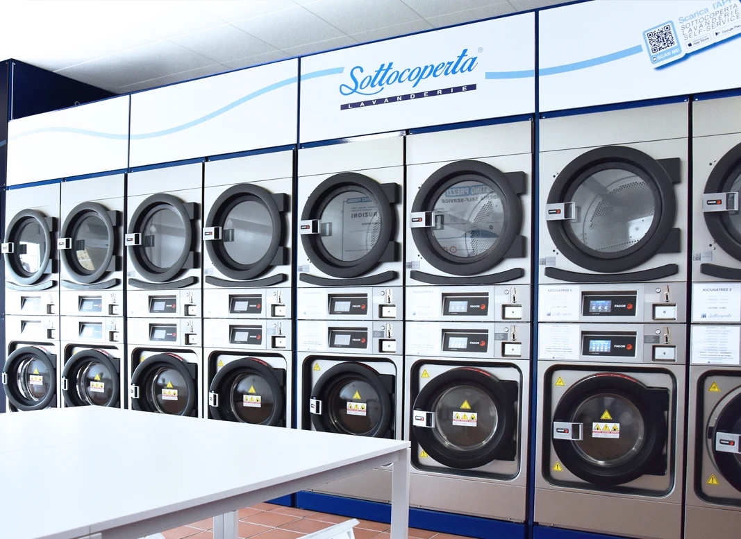 Fila di lavatrici e asciugatrici nella lavanderia self service Sottocoperta